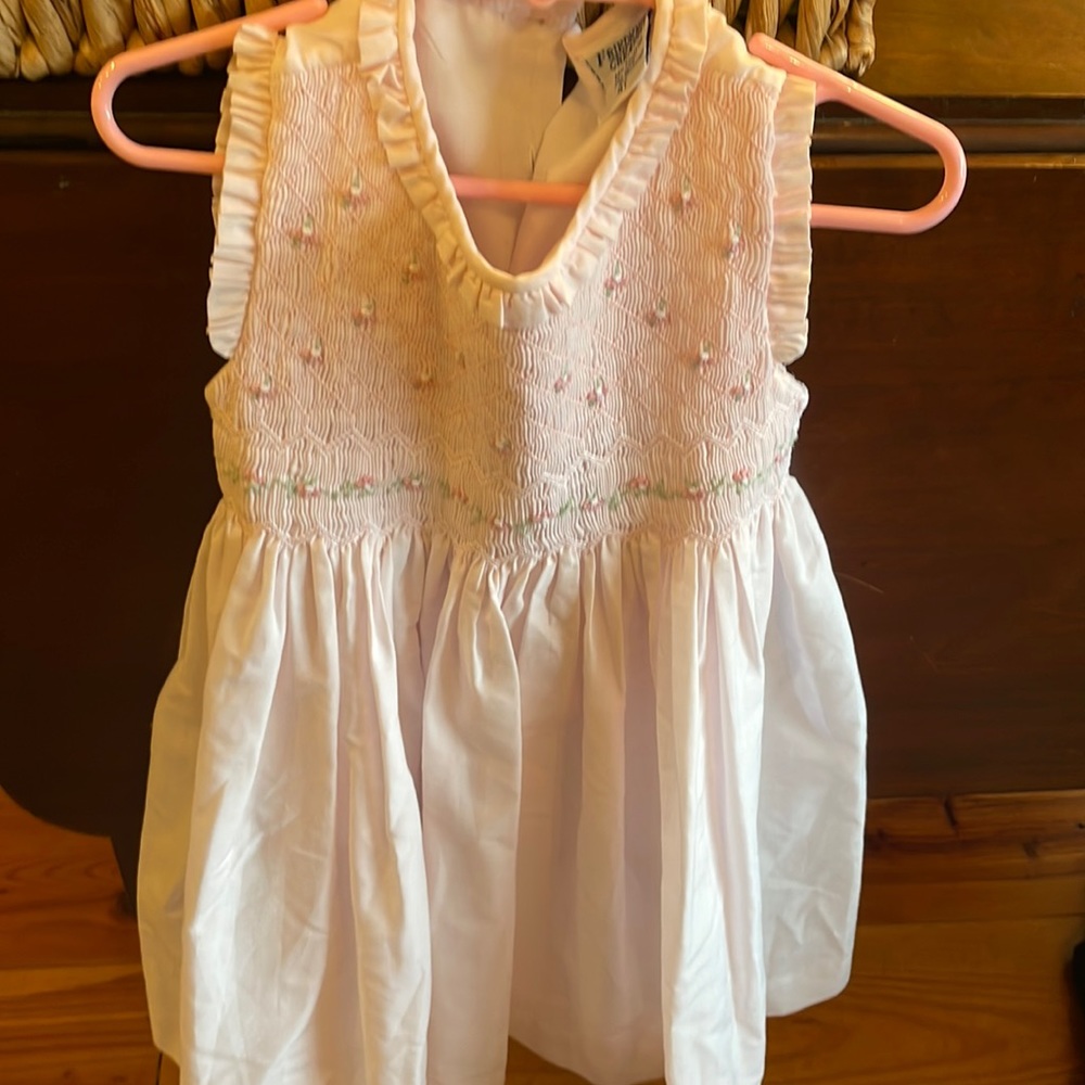 Pale pink smocked dress with flower detail and tie back.